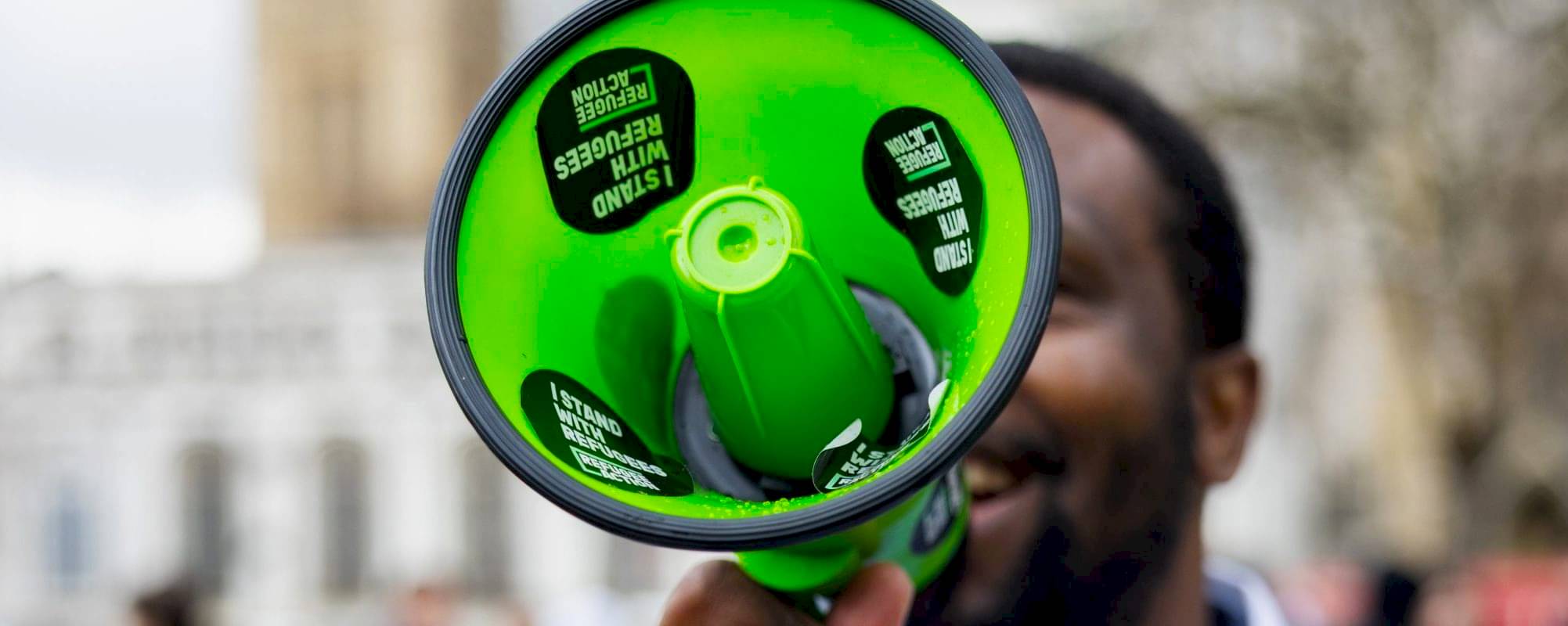 A man holds a megaphone outside parliament. He is shouting down the megaphone.