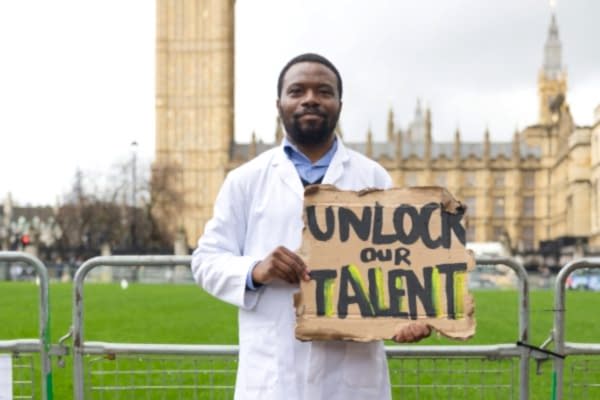 A man stands defiantly in front of Westminster with a sign saying "Unlock our talent"