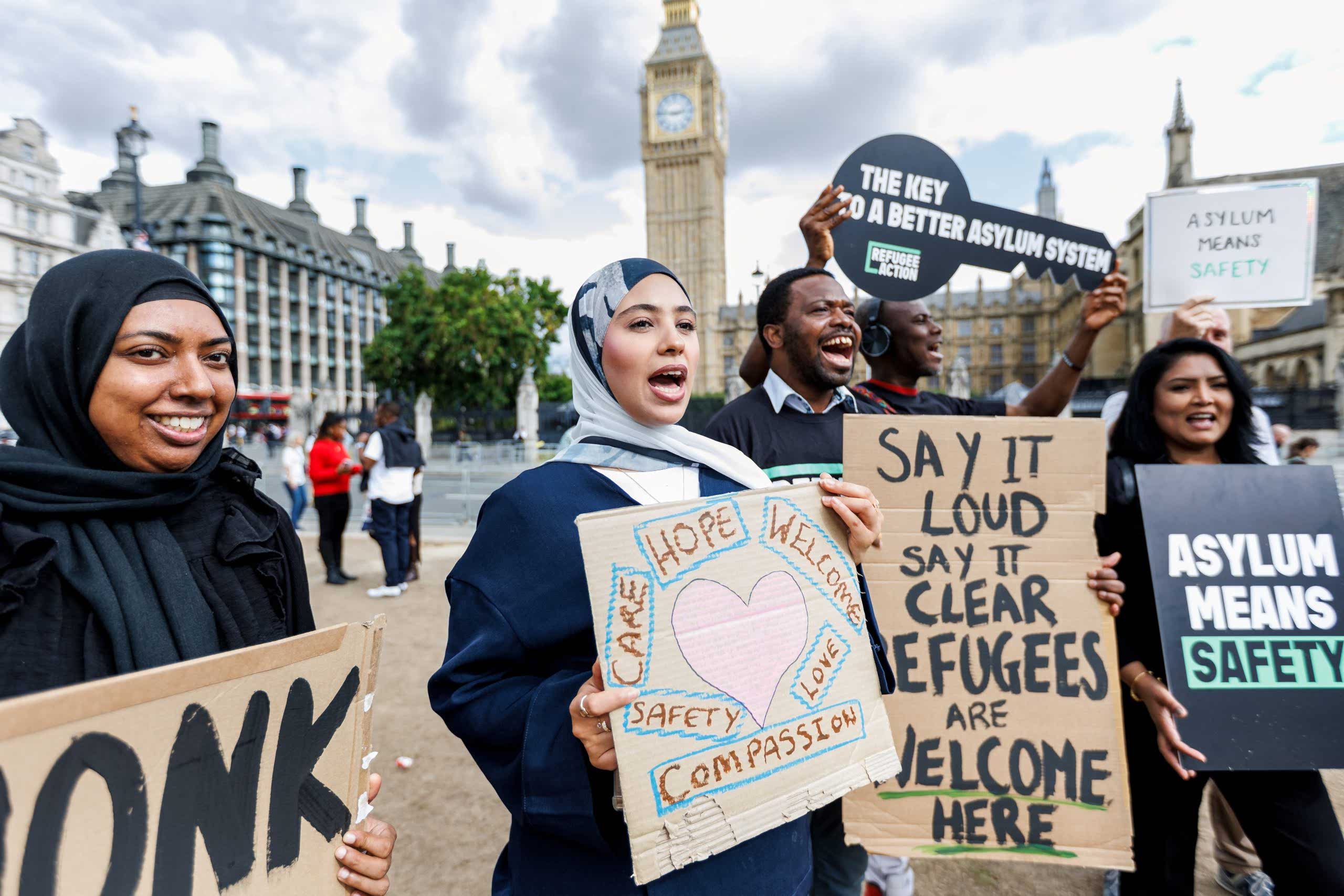 Campaigners cheering outside parliament with signs. One of the says "asylum means safety"